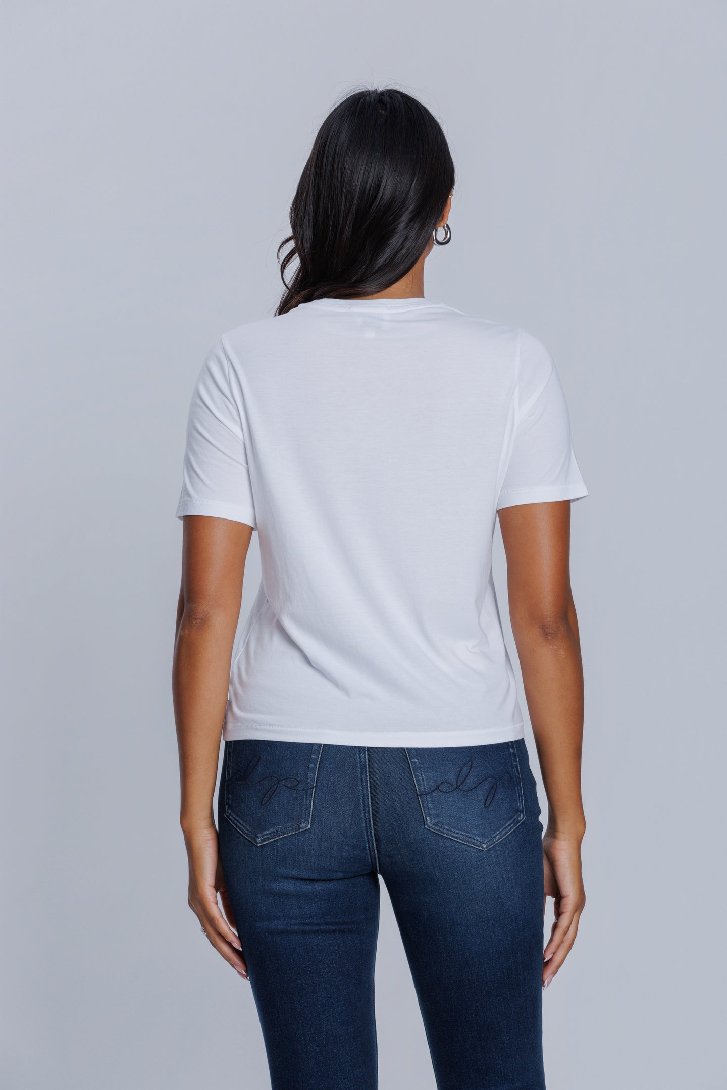 Woman wearing a DePart white t-shirt and dark blue jeans against a light gray background