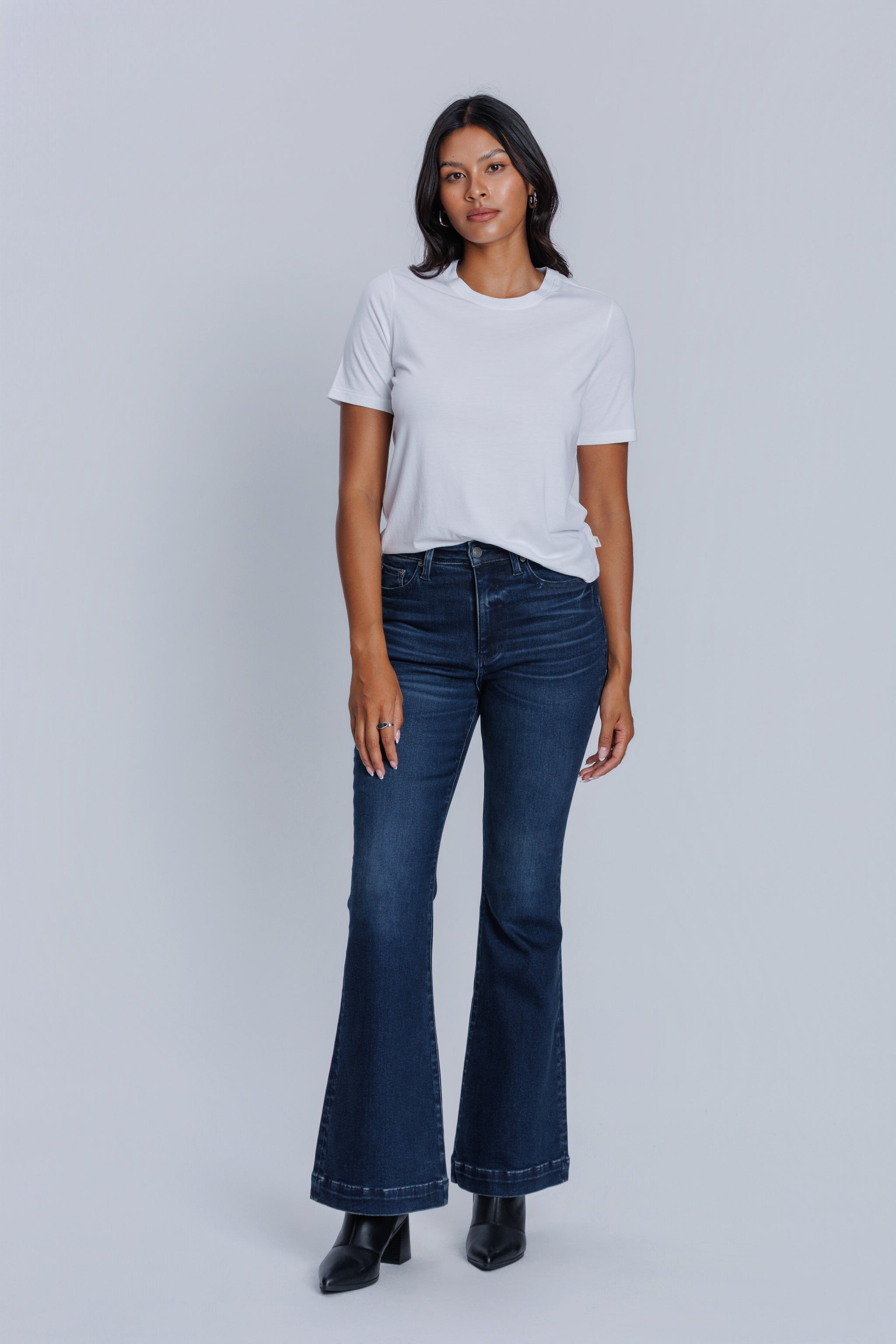 Woman wearing a DePart white crew neck t-shirt and dark blue jeans against a light gray background | model-size: 4