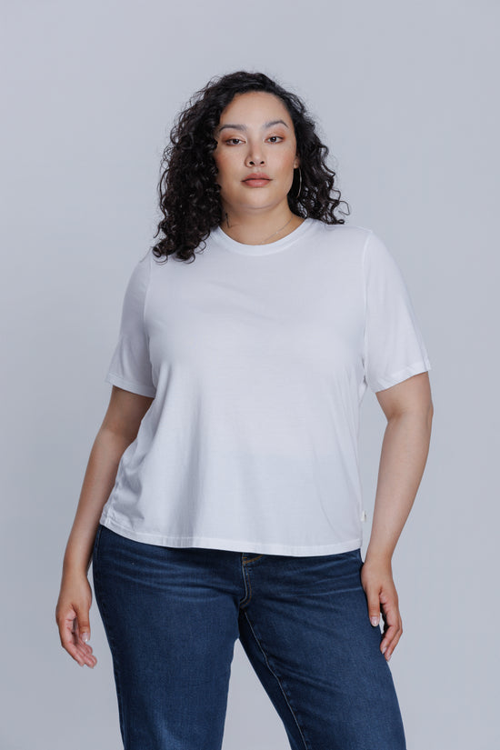 Woman wearing a DePart white t-shirt and dark blue jeans against a light gray background | model-size: 16