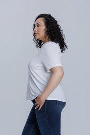Woman wearing a DePart white t-shirt and dark blue jeans against a light gray background