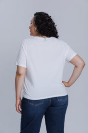 Woman wearing a DePart white t-shirt and dark blue jeans against a light gray background
