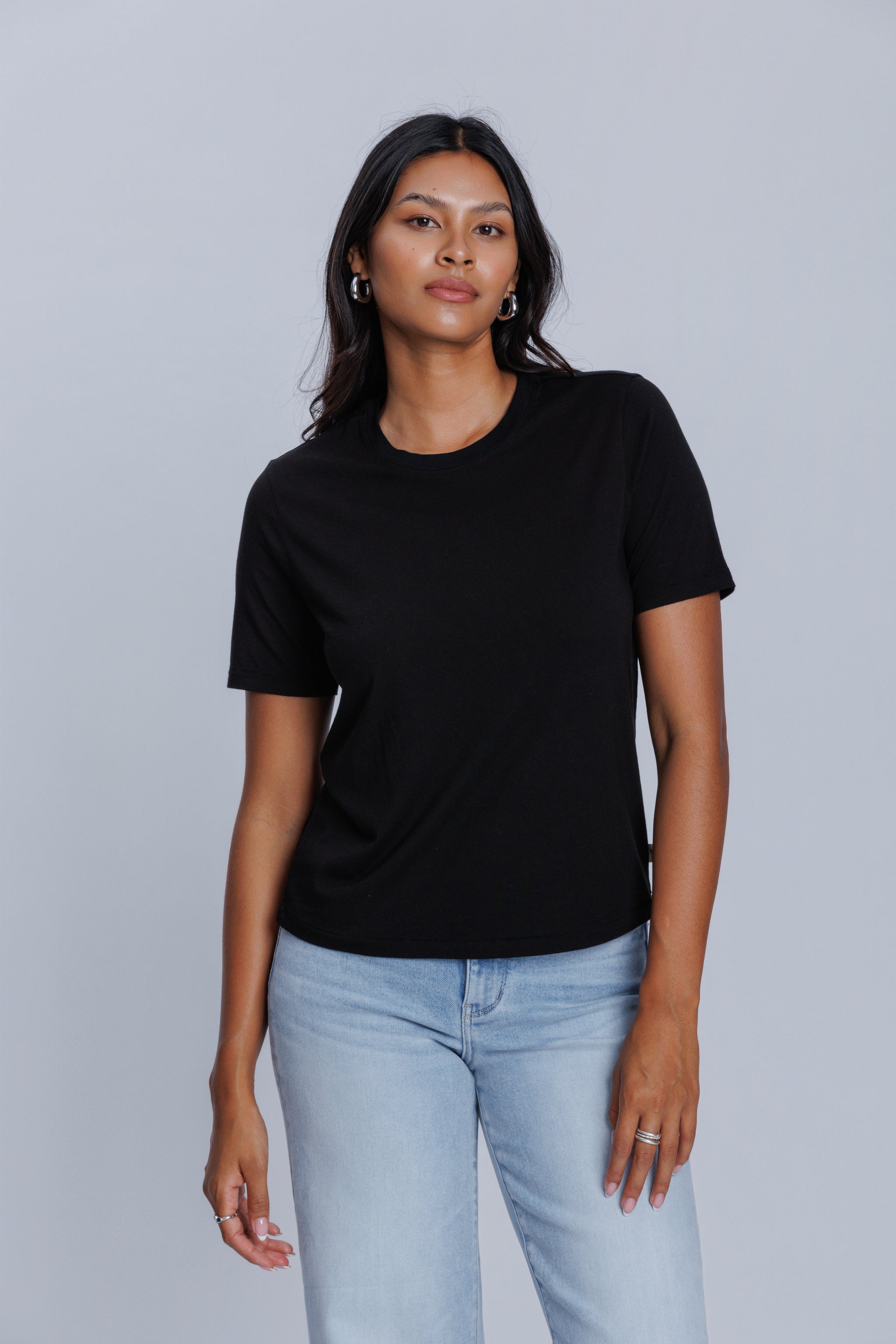 Woman wearing a DePart black t-shirt and light blue jeans against a light gray background | model-size: 4
