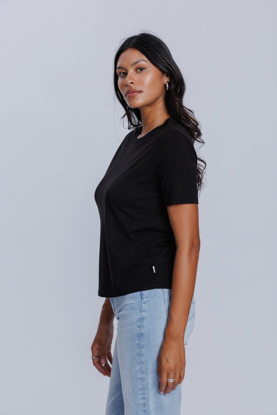 Woman wearing a DePart black t-shirt and light blue jeans against a light gray background