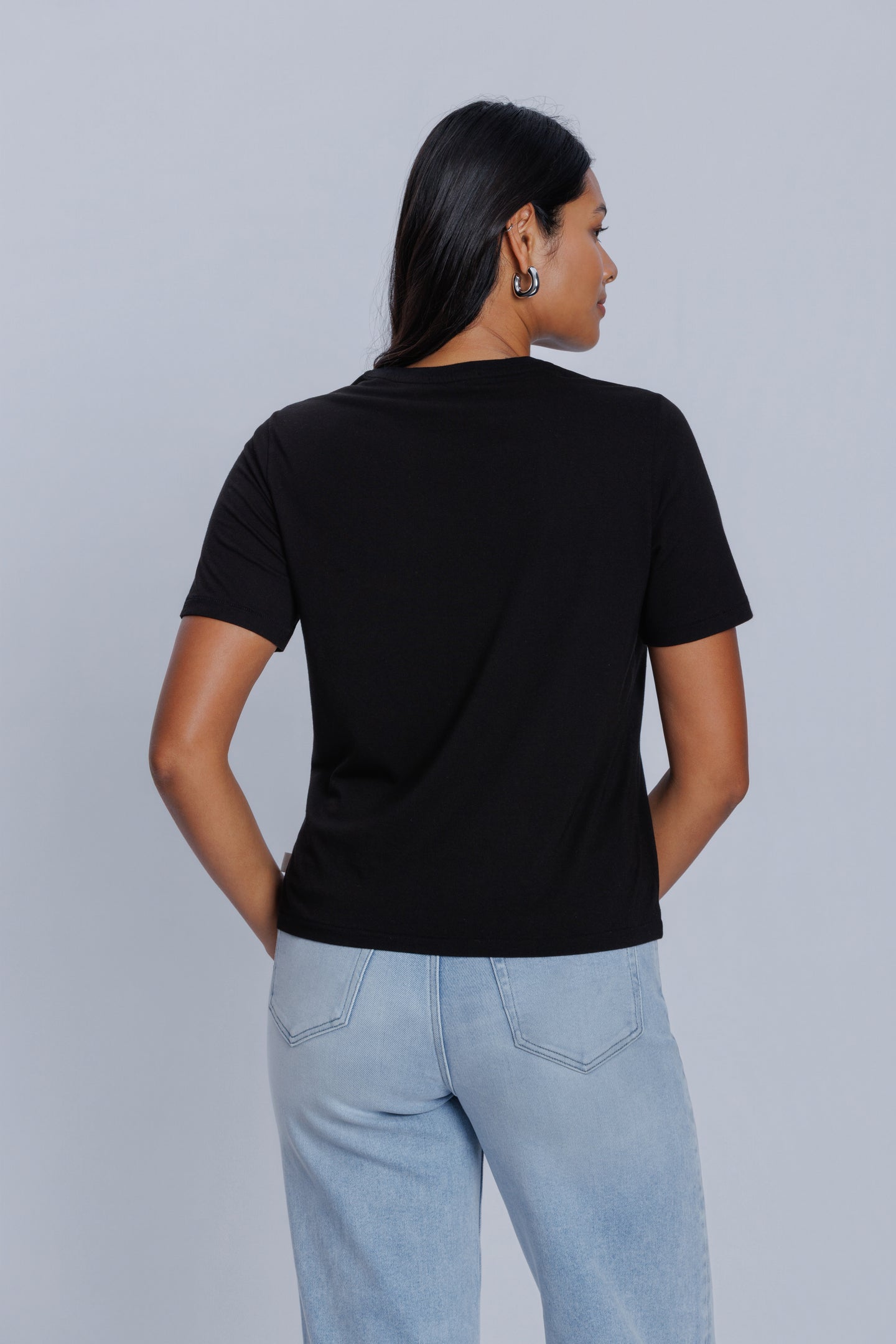 Woman wearing a DePart black t-shirt and light blue jeans against a light gray background