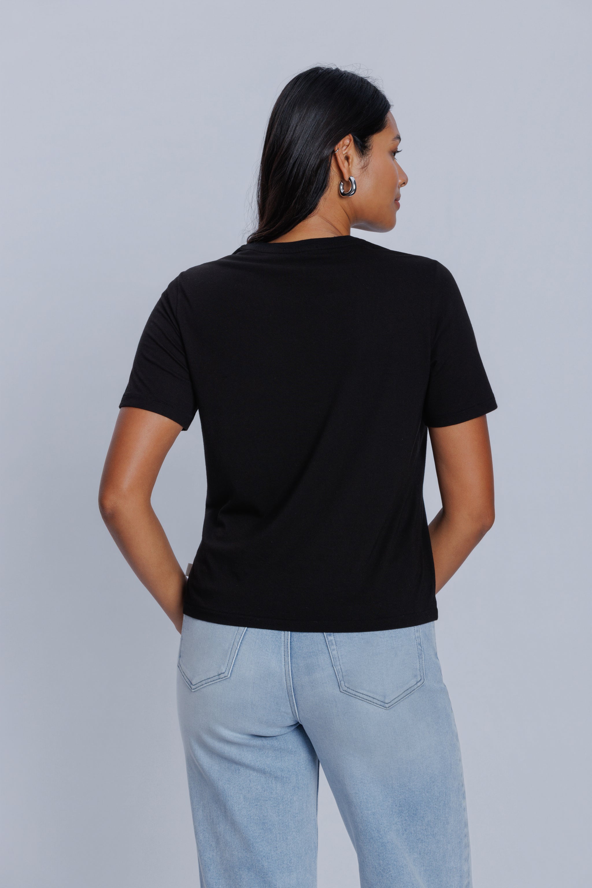 Woman wearing a DePart black t-shirt and light blue jeans against a light gray background