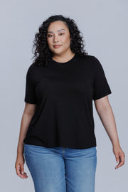 Woman wearing a DePart black t-shirt and blue jeans against a light gray background | model-size: 16
