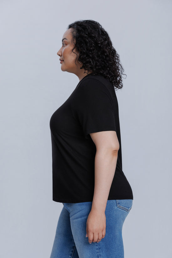 Woman wearing a DePart black t-shirt and blue jeans against a light gray background