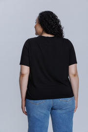 Woman wearing a DePart black t-shirt and blue jeans against a light gray background