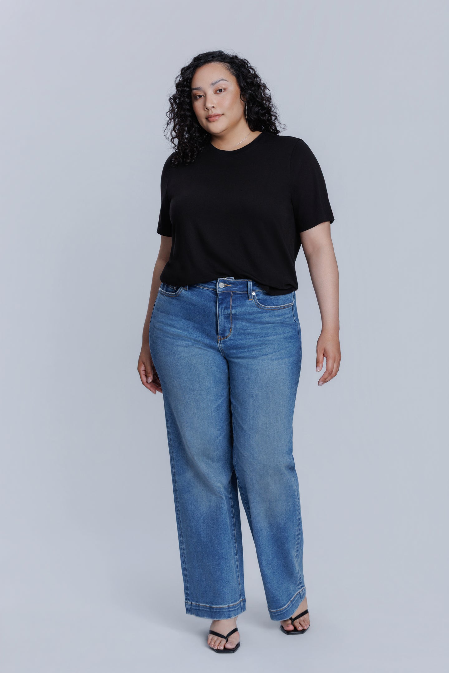 Woman wearing a DePart black crew neck t-shirt and blue jeans against a light gray background | model-size: 16