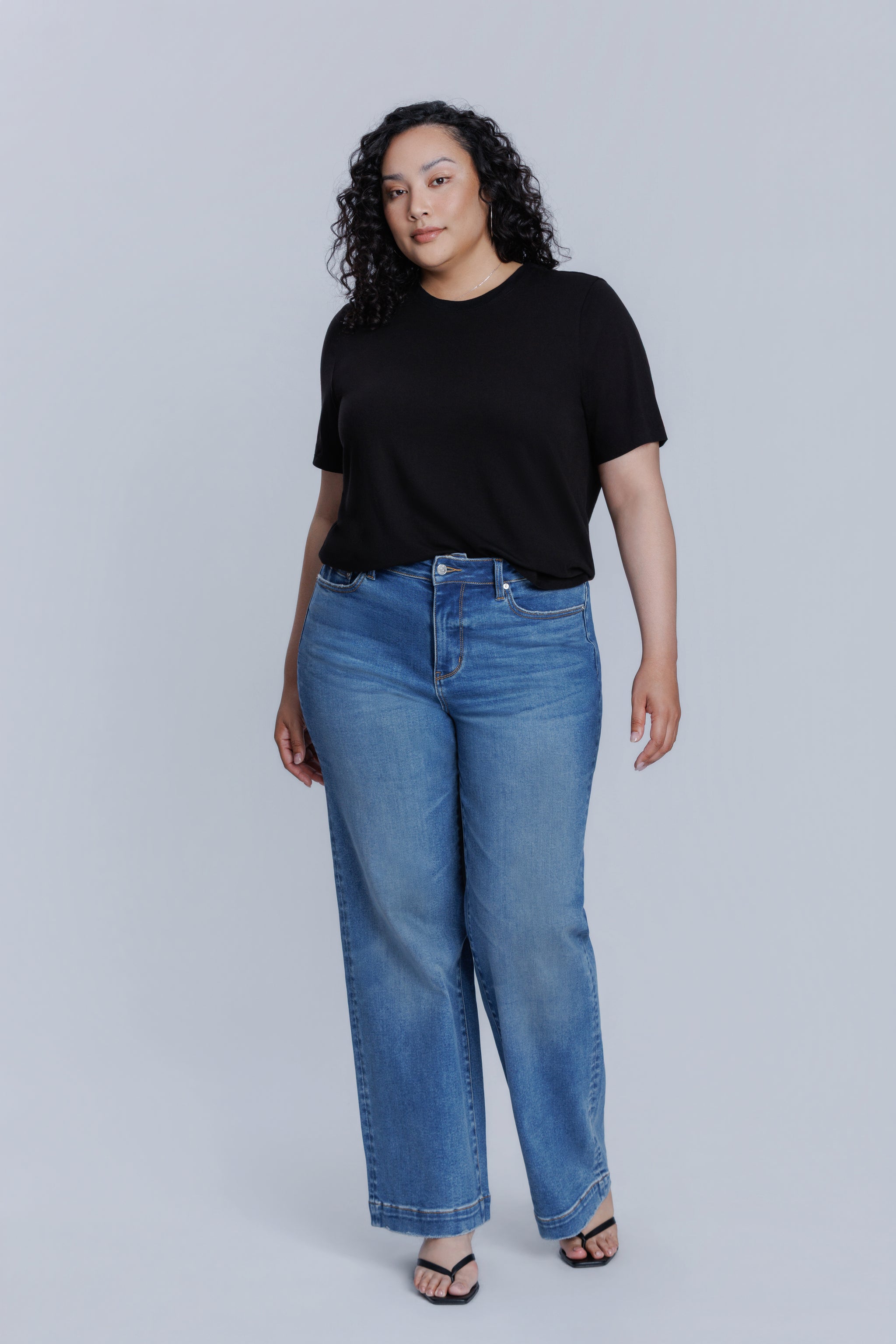 Woman wearing a DePart black crew neck t-shirt and blue jeans against a light gray background | model-size: 16
