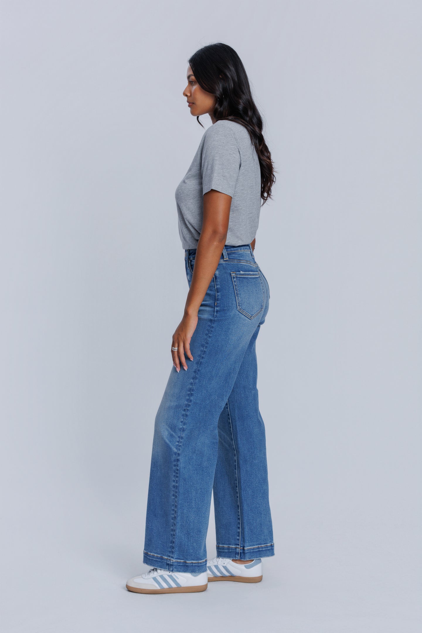 Woman wearing a DePart gray crew neck t-shirt and blue jeans against a light gray background