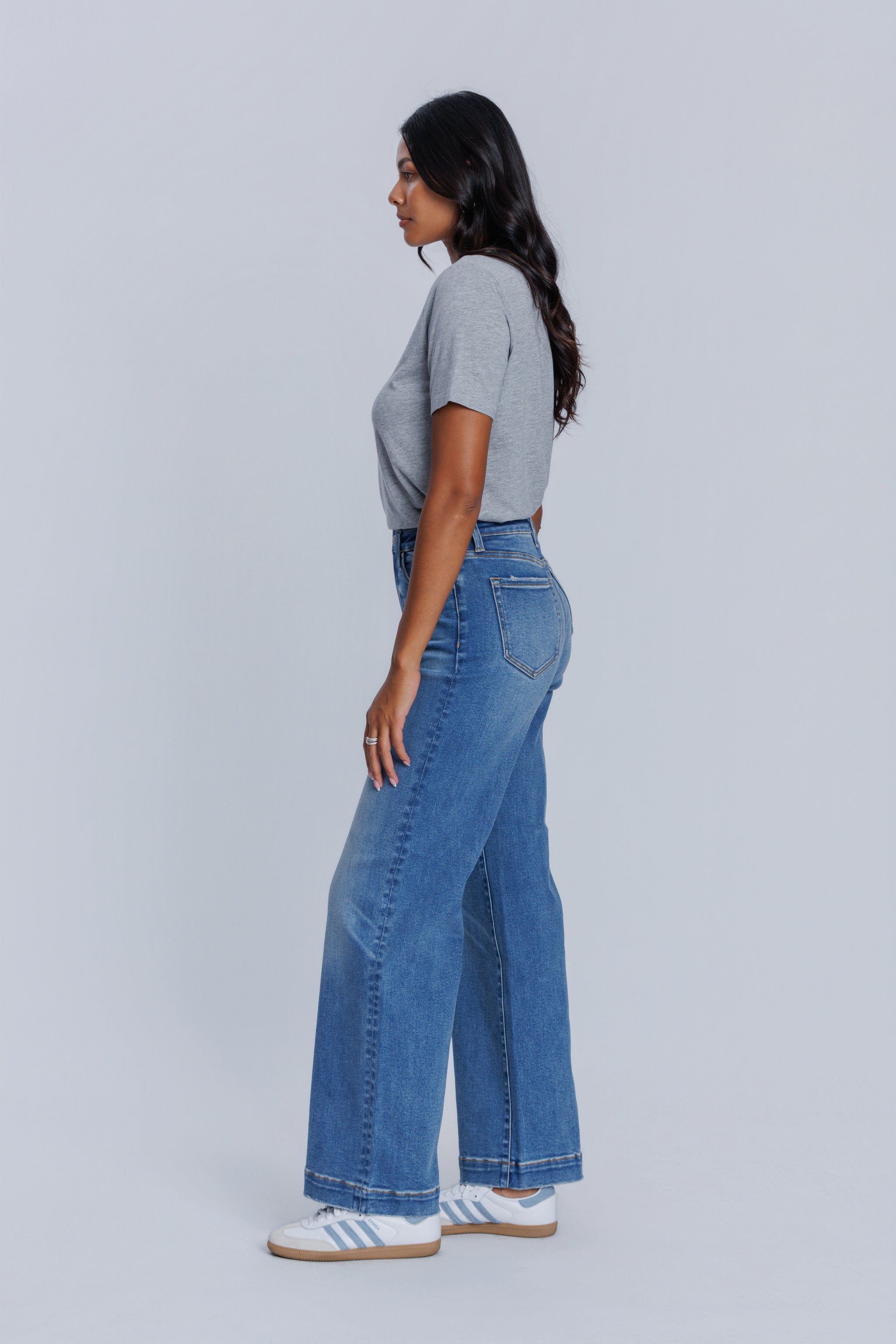 Woman wearing a DePart gray crew neck t-shirt and blue jeans against a light gray background