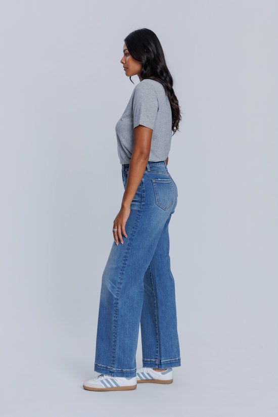Woman wearing a DePart gray crew neck t-shirt and blue jeans against a light gray background
