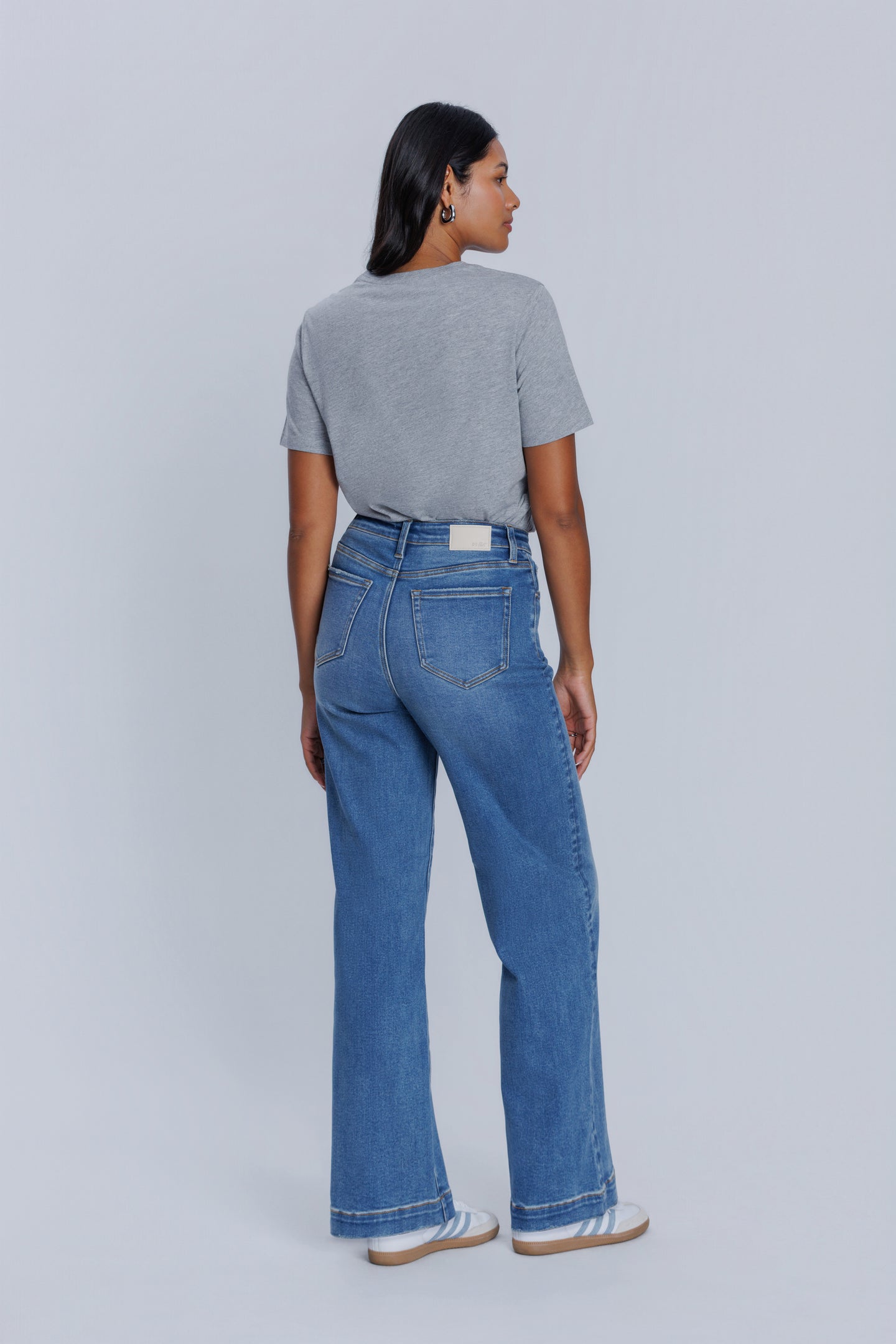 Woman wearing a DePart gray crew neck t-shirt and blue jeans against a light gray background