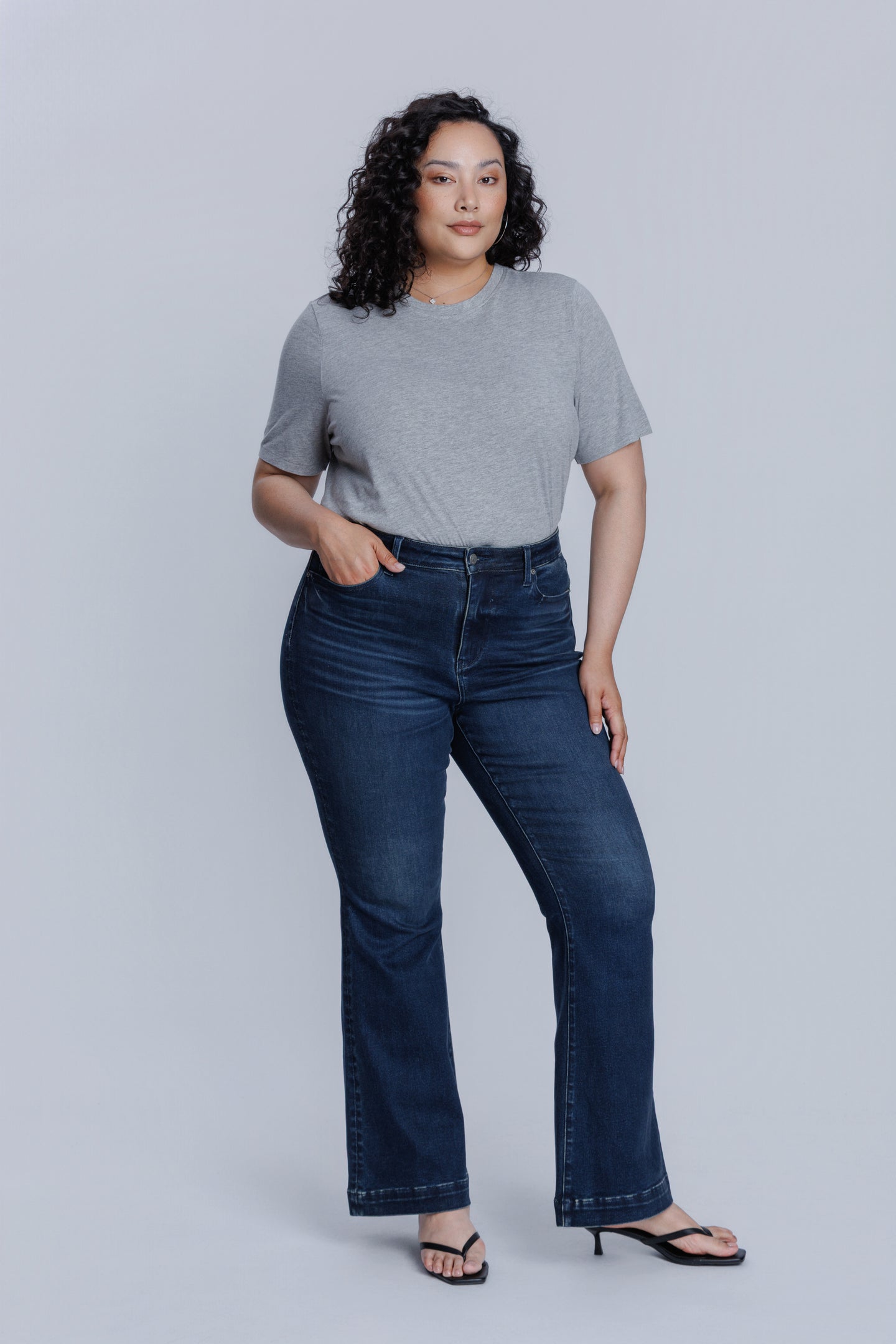 Woman wearing a DePart gray crew neck t-shirt and dark blue jeans against a light gray background | model-size: 16