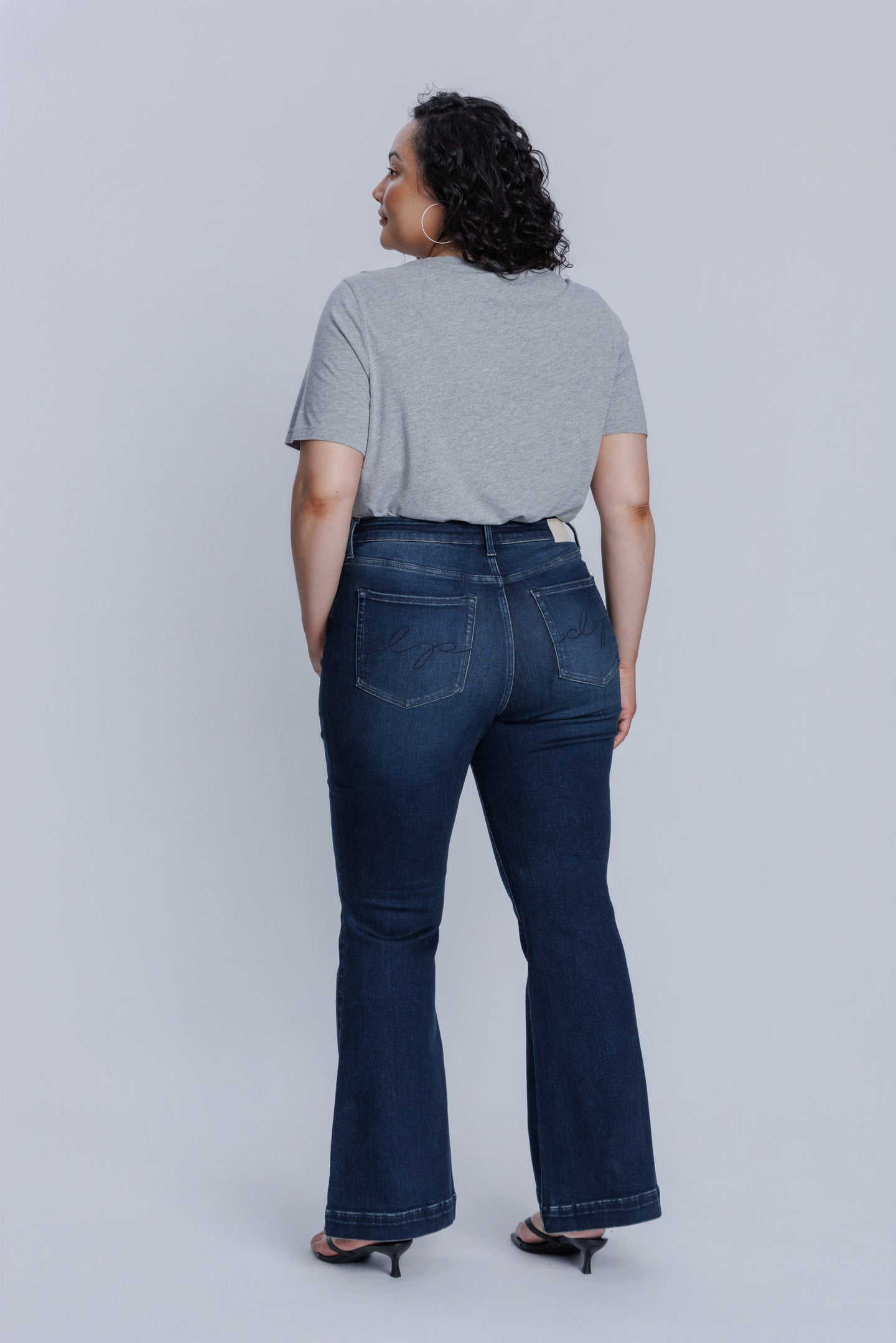 Woman wearing a DePart gray crew neck t-shirt and dark blue jeans against a light gray background