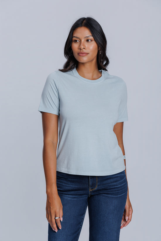 Woman wearing a DePart light blue t-shirt and dark blue jeans against a light gray background | model-size: 4
