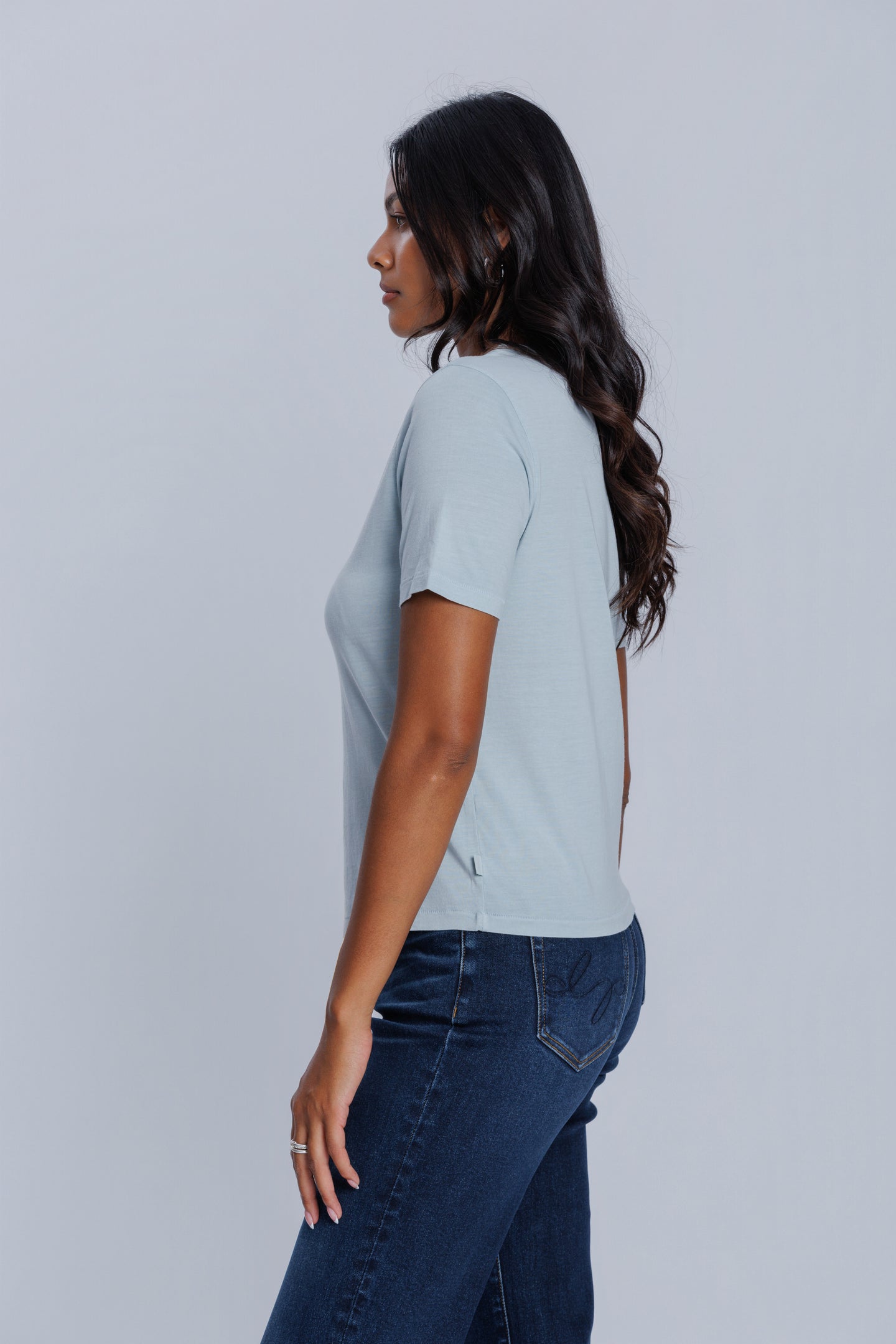 Woman wearing a DePart light blue t-shirt and dark blue jeans against a light gray background