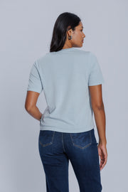 Woman wearing a DePart light blue t-shirt and dark blue jeans against a light gray background