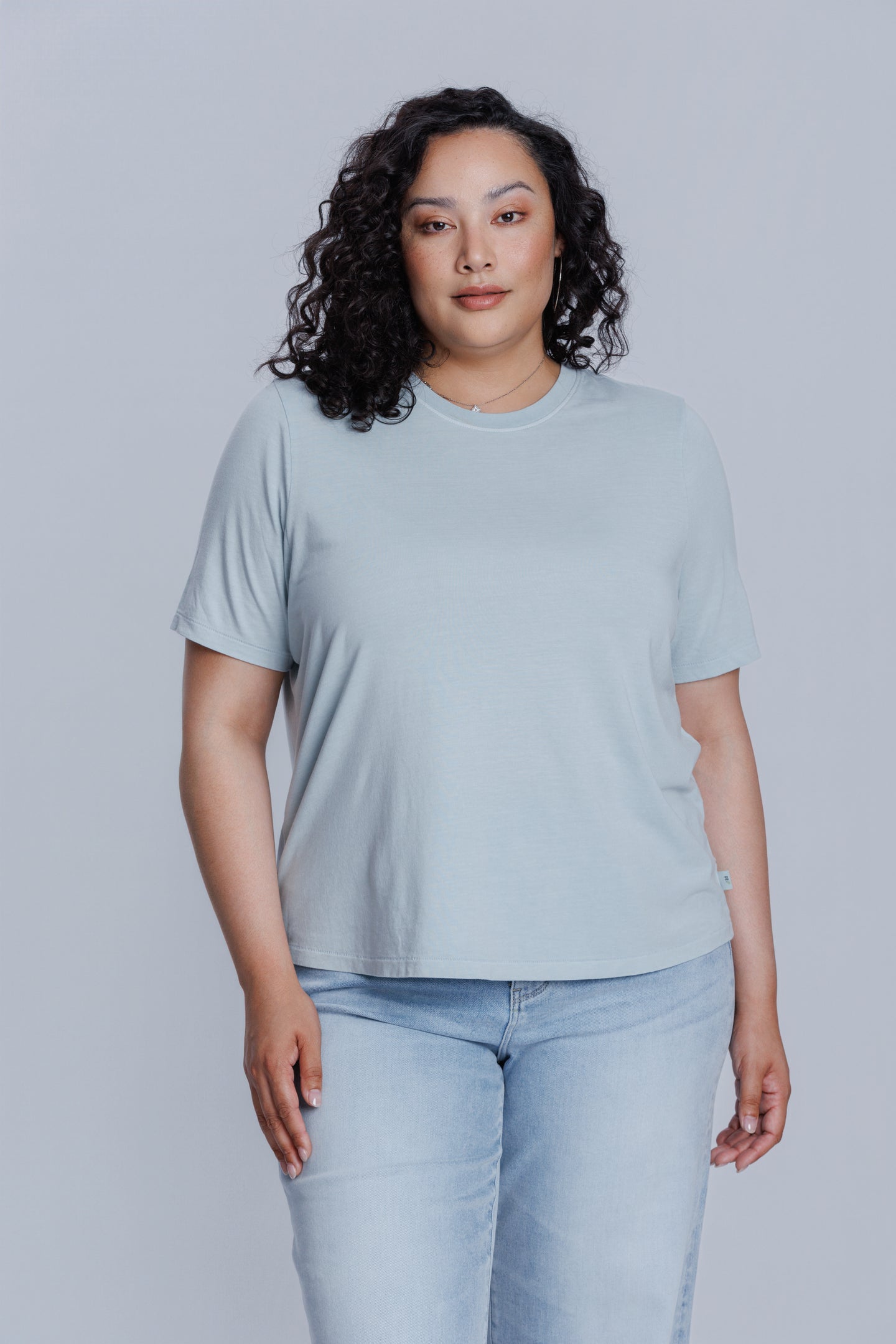 Woman wearing a DePart light blue t-shirt and light blue jeans against a light gray background | model-size: 16