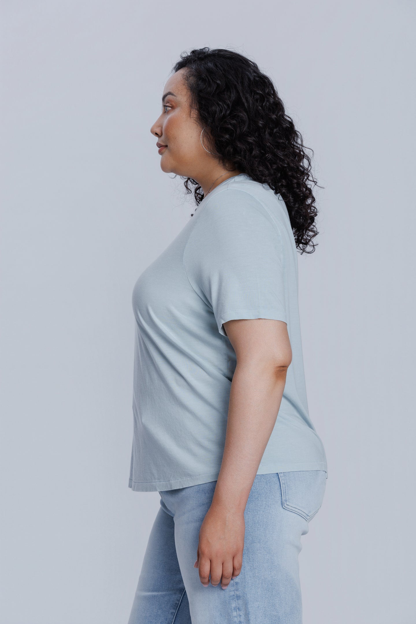 Woman wearing a DePart light blue t-shirt and light blue jeans against a light gray background