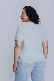 Woman wearing a DePart light blue t-shirt and light blue jeans against a light gray background