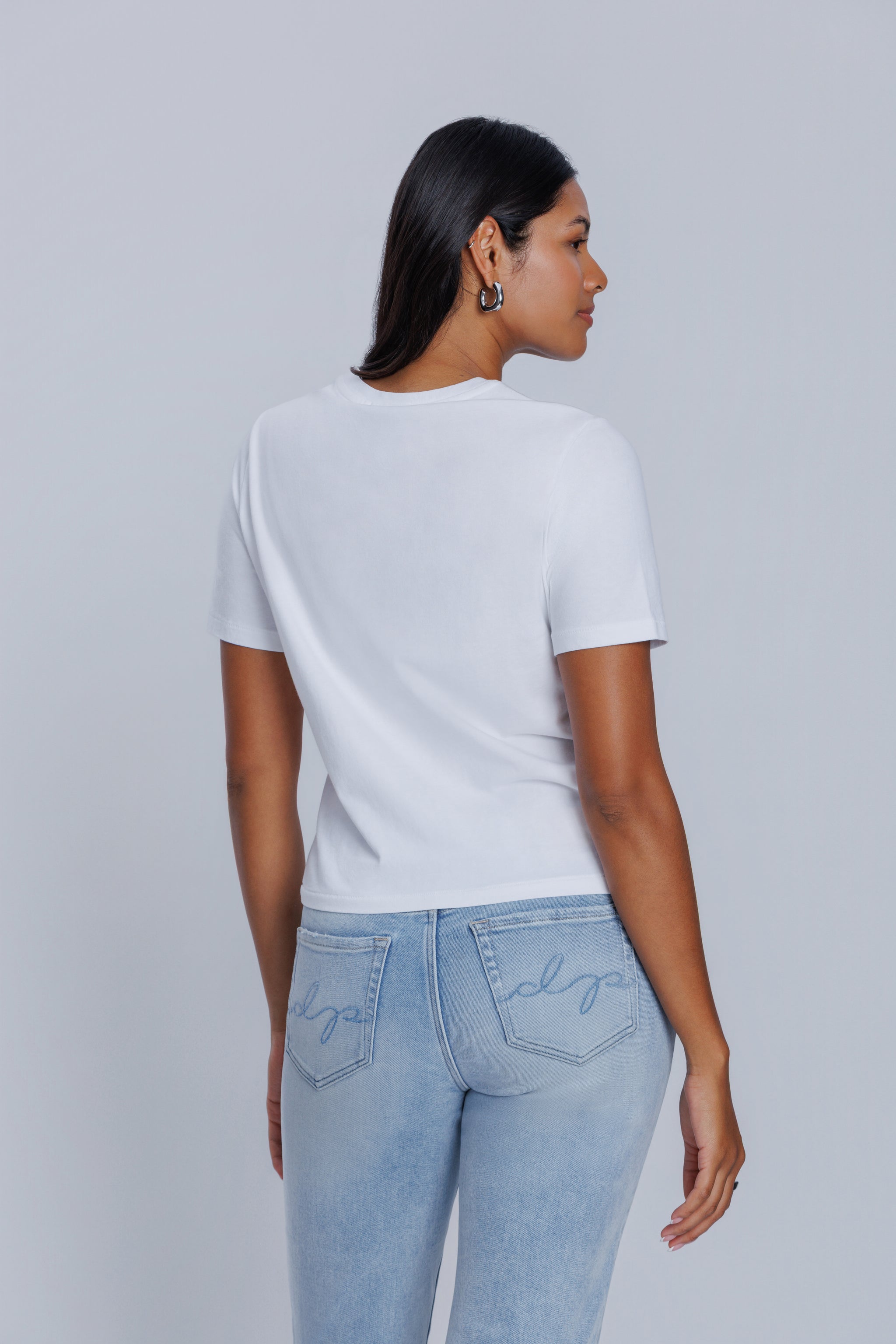 Woman wearing a DePart white t-shirt and light blue jeans against a light gray background