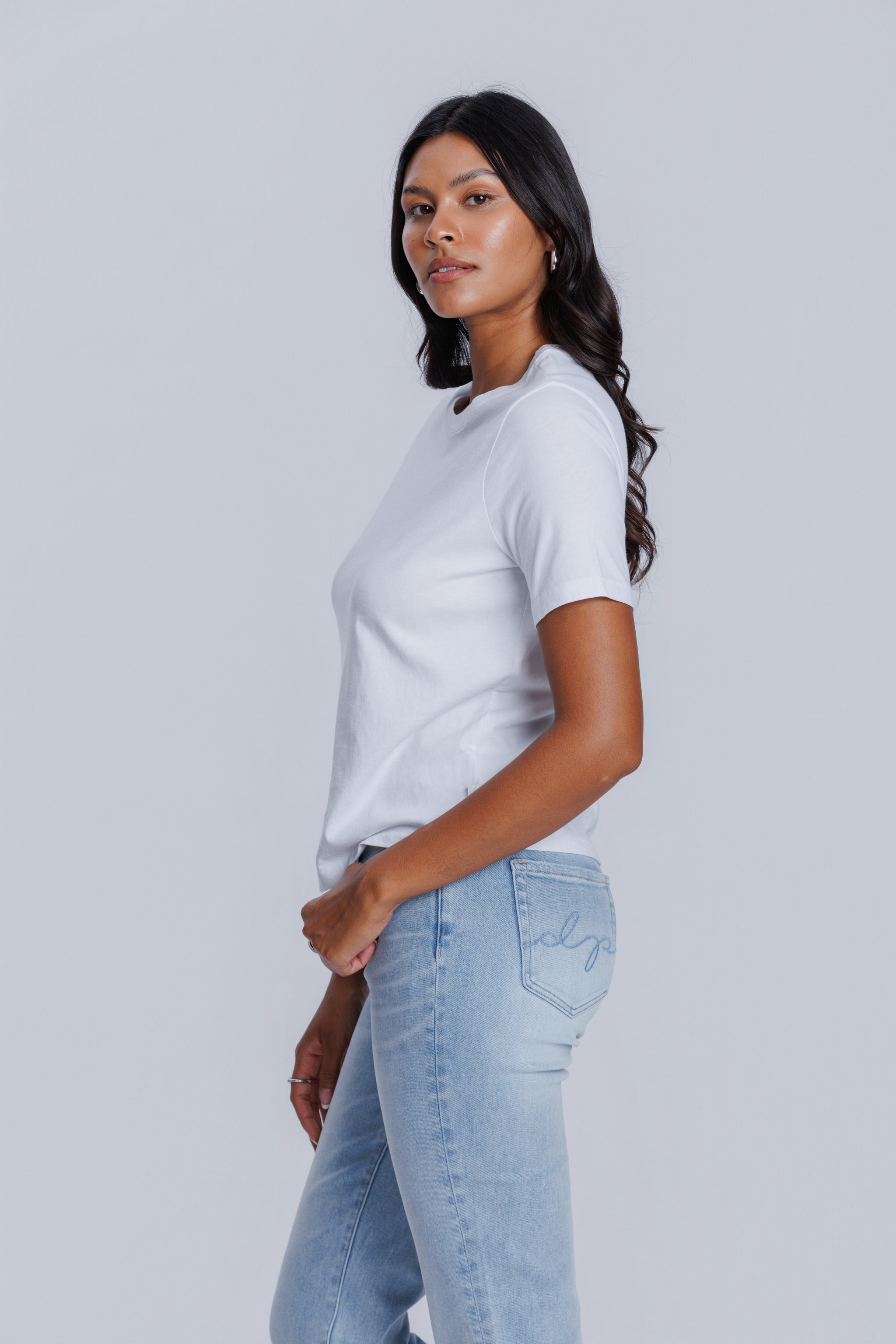 Woman wearing a DePart white t-shirt and light blue jeans against a light gray background