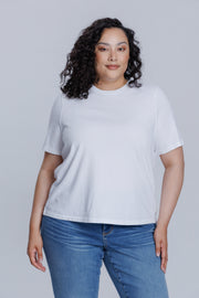 Woman wearing a DePart white t-shirt and blue jeans against a light gray background | model-size: 16