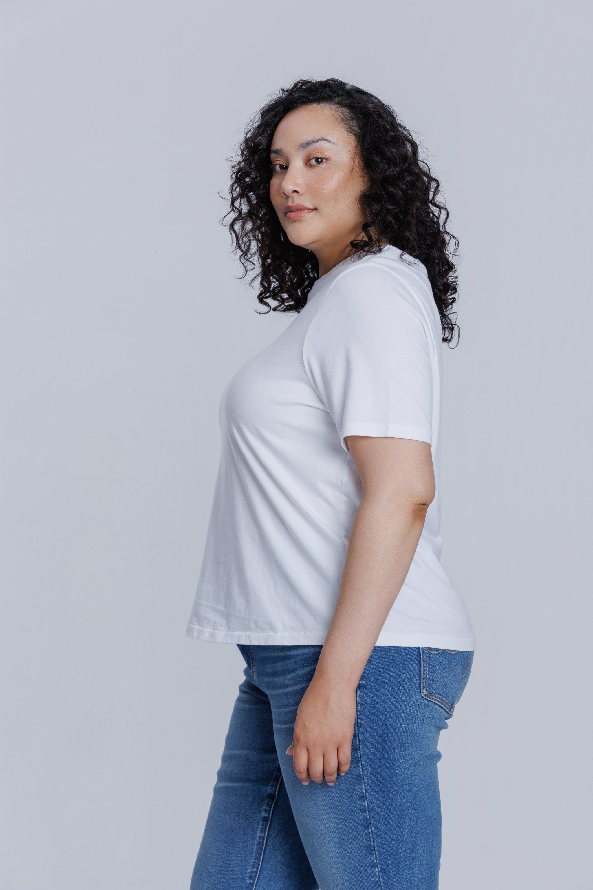 Woman wearing a DePart white t-shirt and blue jeans against a light gray background