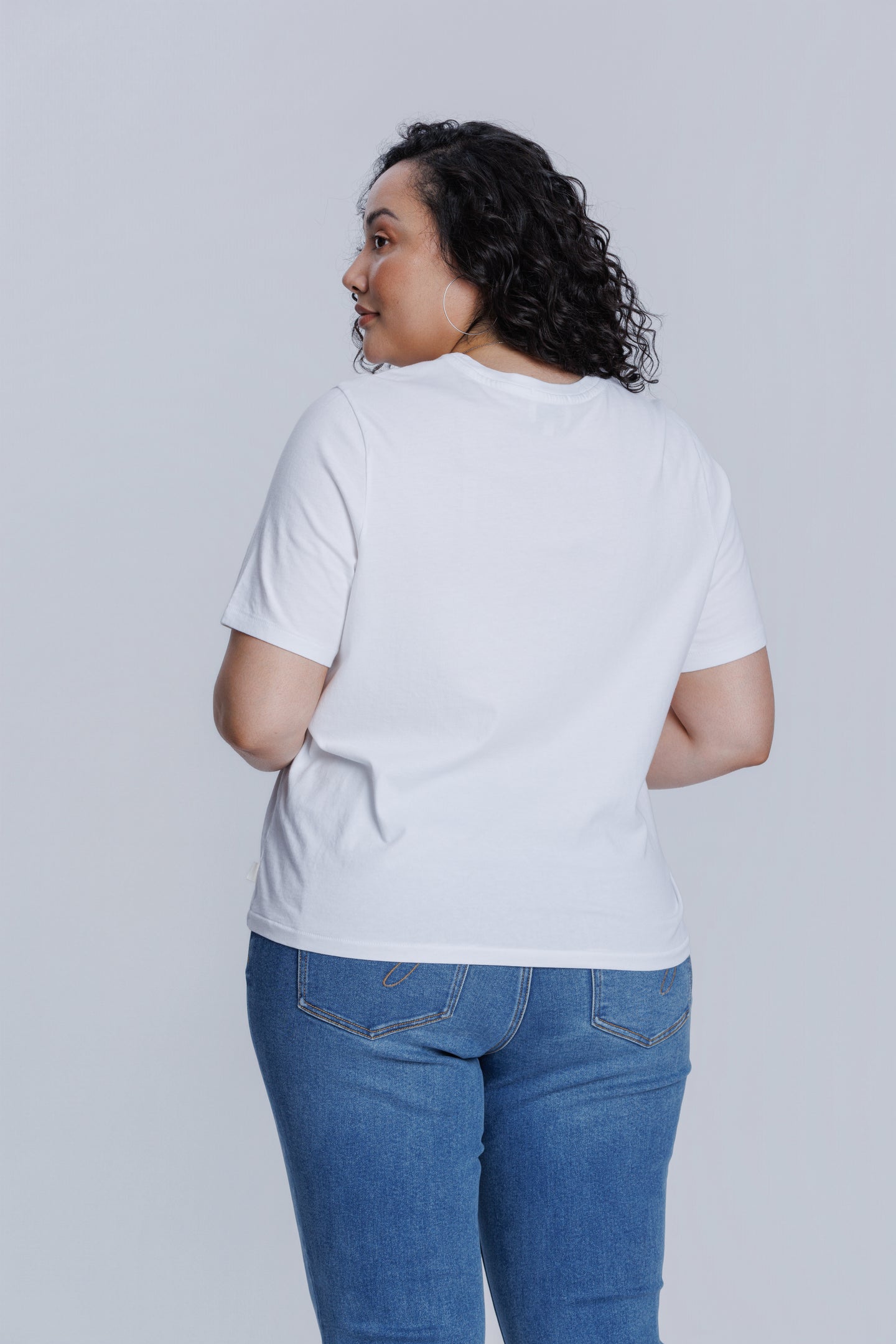 Woman wearing a DePart white t-shirt and blue jeans against a light gray background