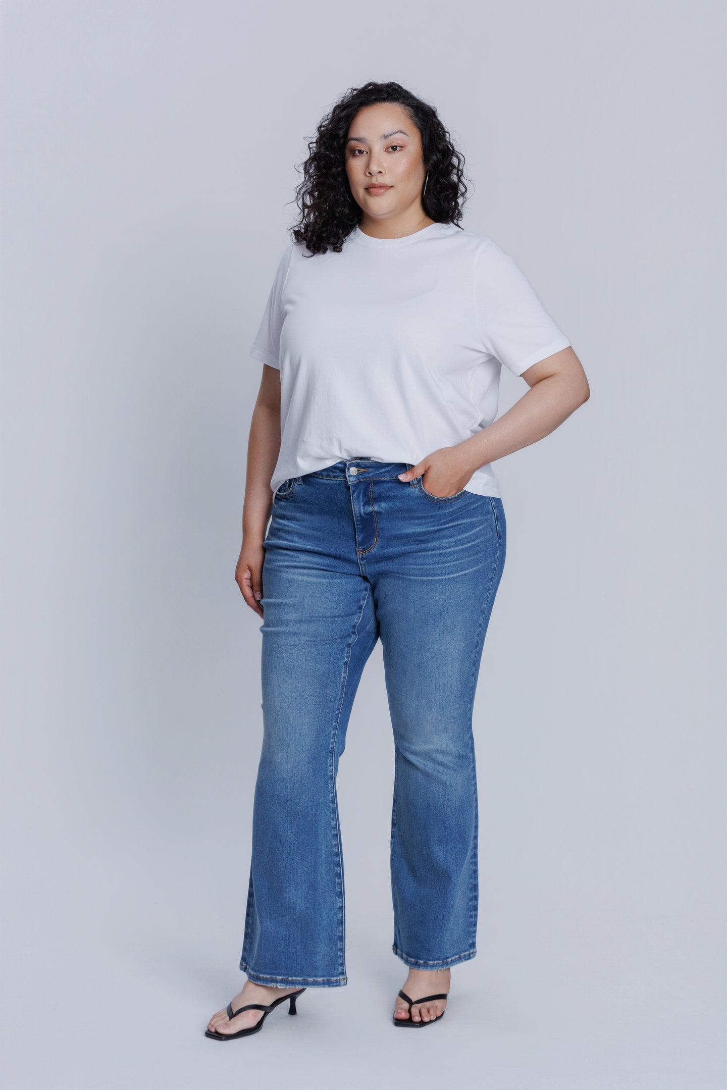 Woman wearing a DePart white t-shirt and blue flare jeans against a light gray background | model-size: 16