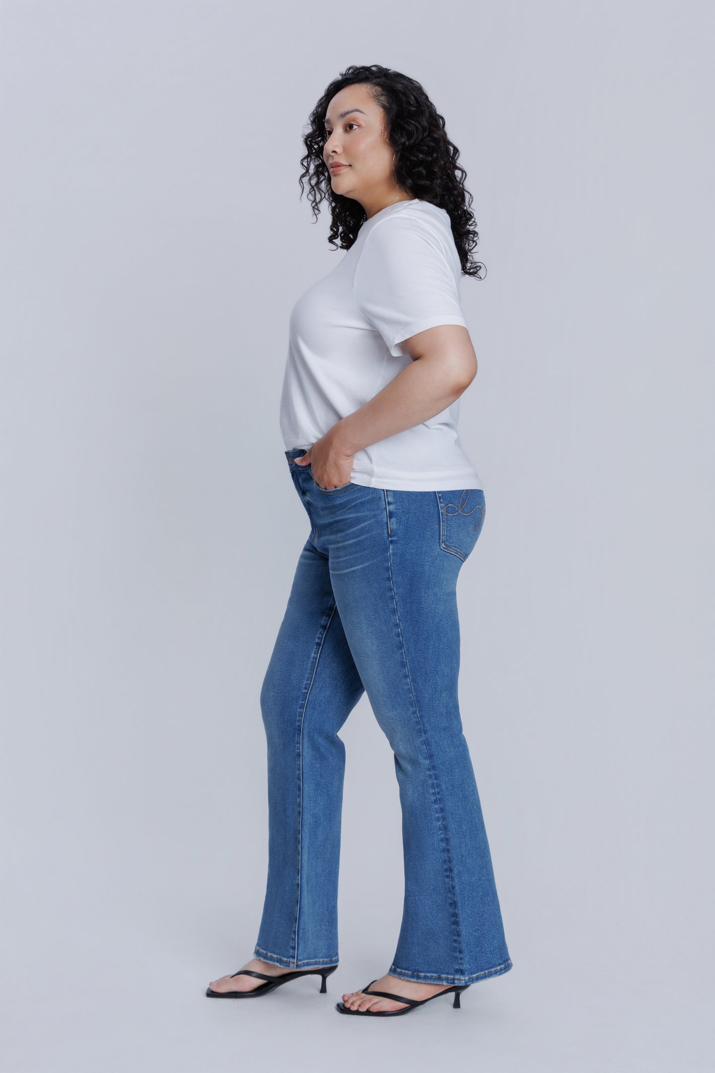 Woman wearing a DePart white t-shirt and blue flare jeans against a light gray background