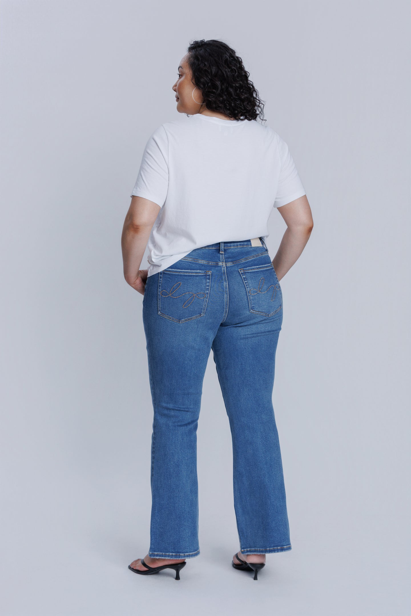 Woman wearing a DePart white t-shirt and blue flare jeans against a light gray background