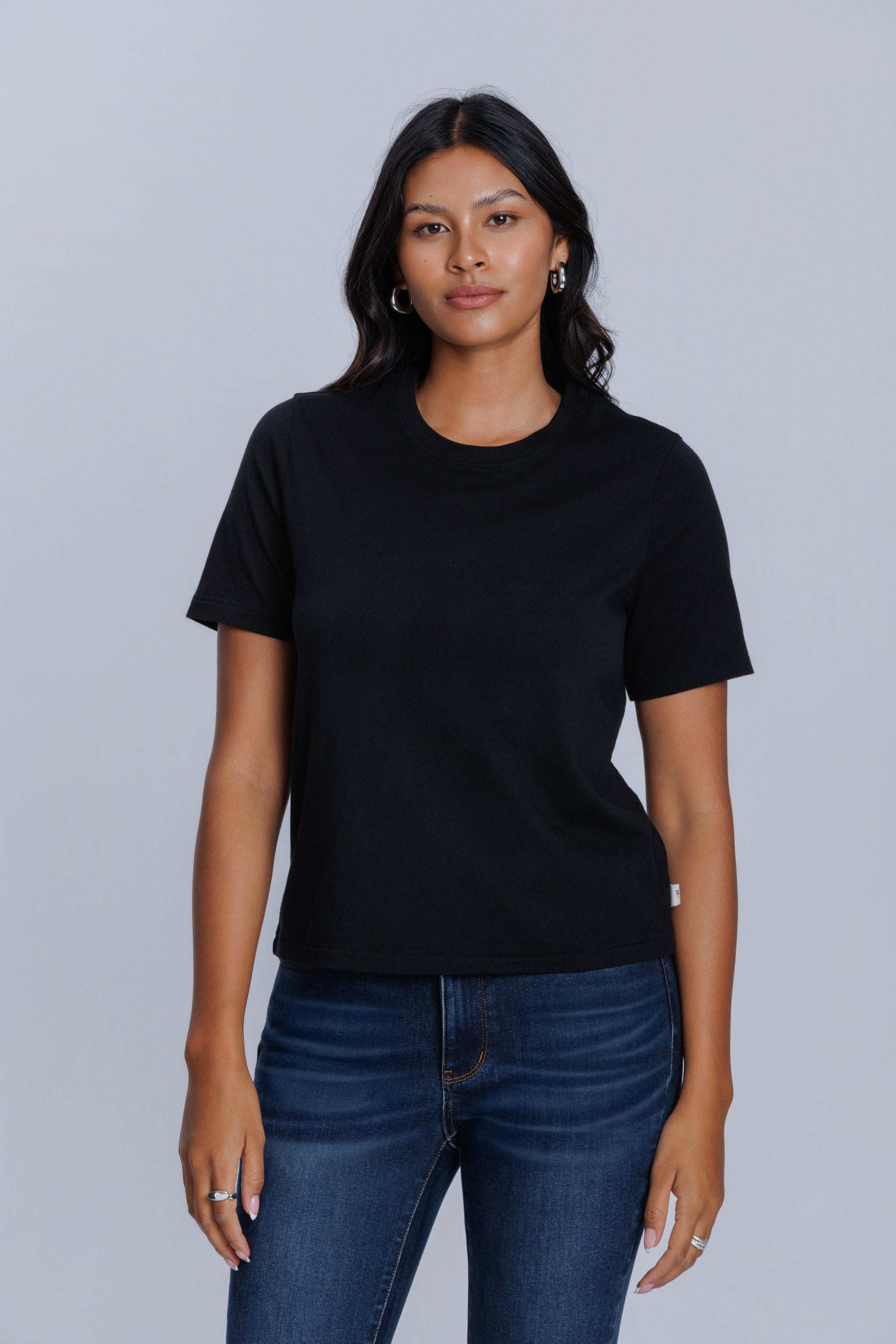Woman wearing a DePart black t-shirt and dark blue jeans against a light gray background | model-size: 4