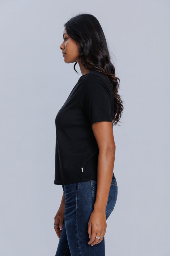 Woman wearing a DePart black t-shirt and dark blue jeans against a light gray background