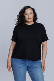 Woman wearing a DePart black t-shirt and blue jeans against a light gray background | model-size: 16