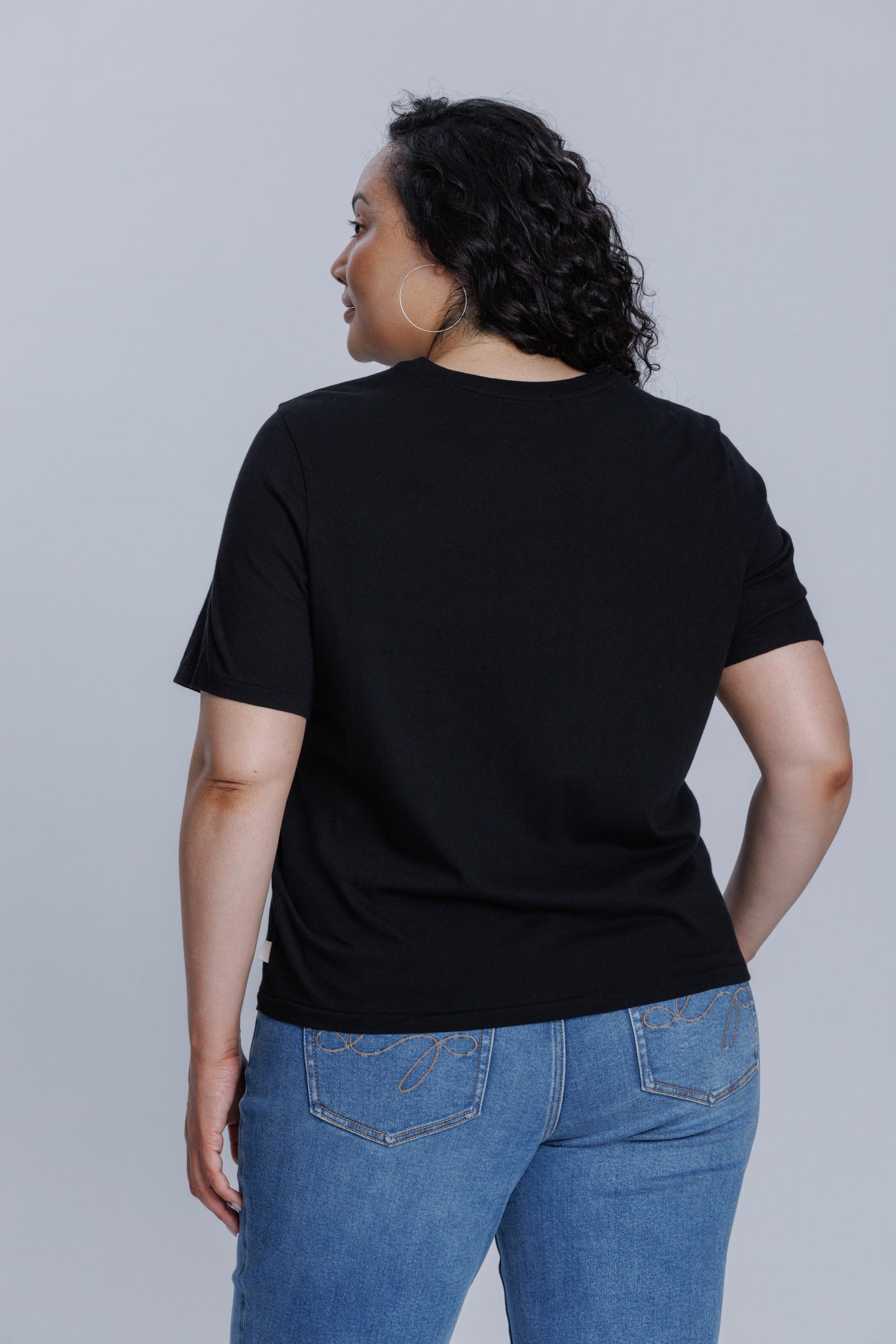 Woman wearing a DePart black t-shirt and blue jeans against a light gray background