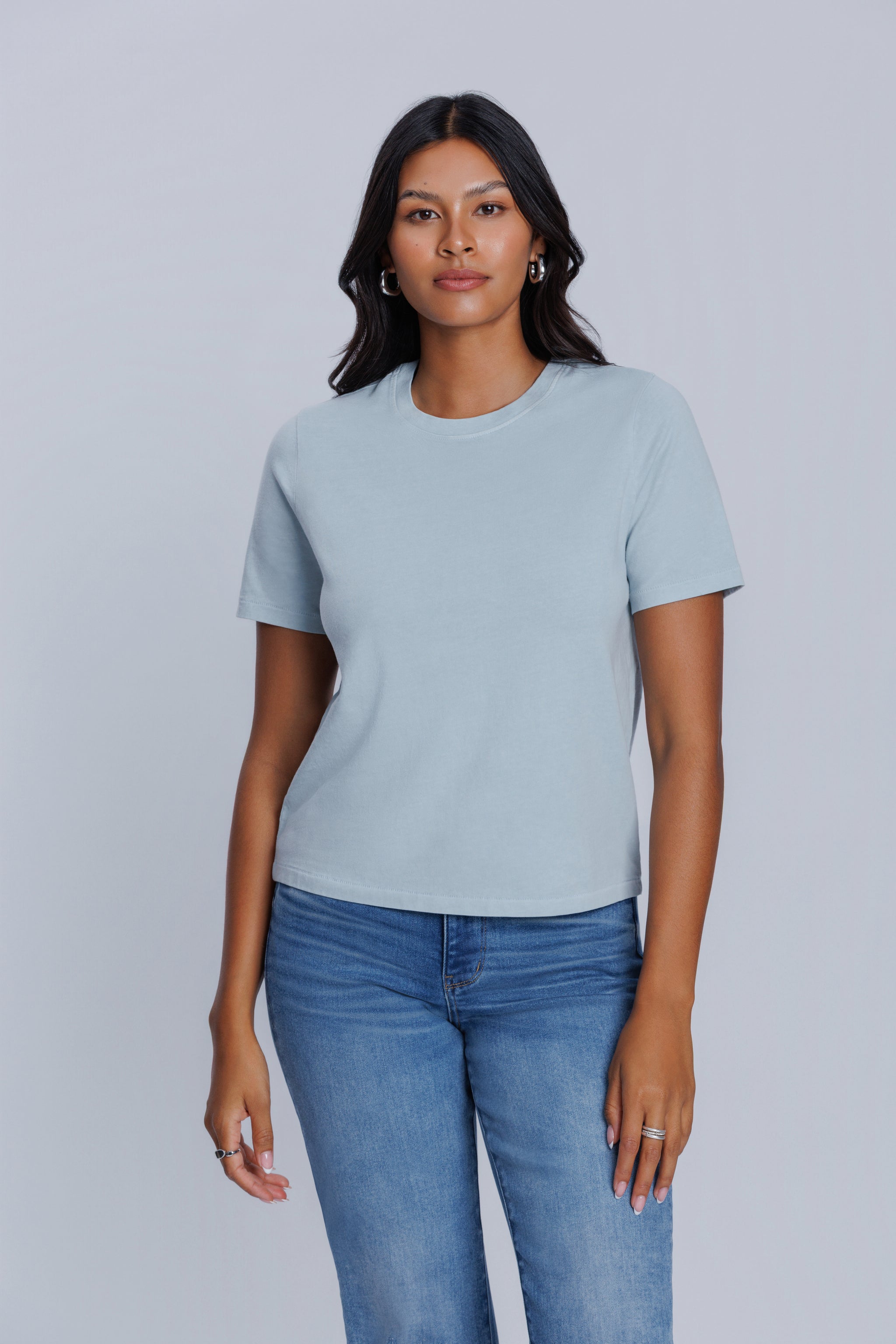 Woman wearing a DePart light blue t-shirt and blue jeans against a light gray background | model-size: 4
