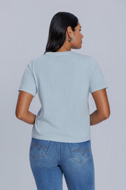 Woman wearing a DePart light blue t-shirt and blue jeans against a light gray background