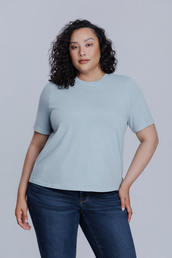 Woman wearing a DePart blue t-shirt and dark blue jeans against a light gray background | model-size: 16