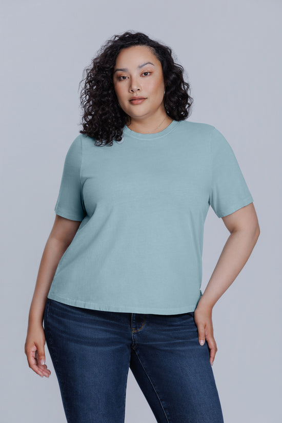 Woman wearing a DePart blue t-shirt and dark blue jeans against a light gray background | model-size: 16