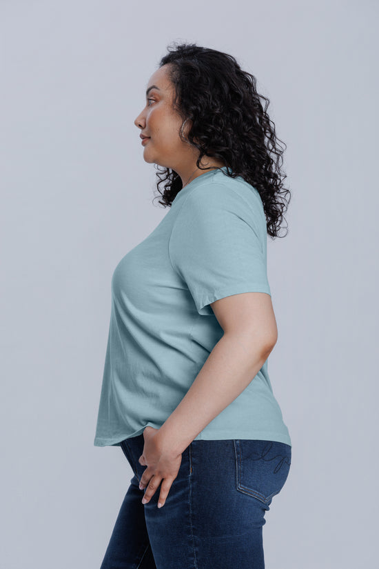 Woman wearing a light blue t-shirt and dark jeans against a plain background