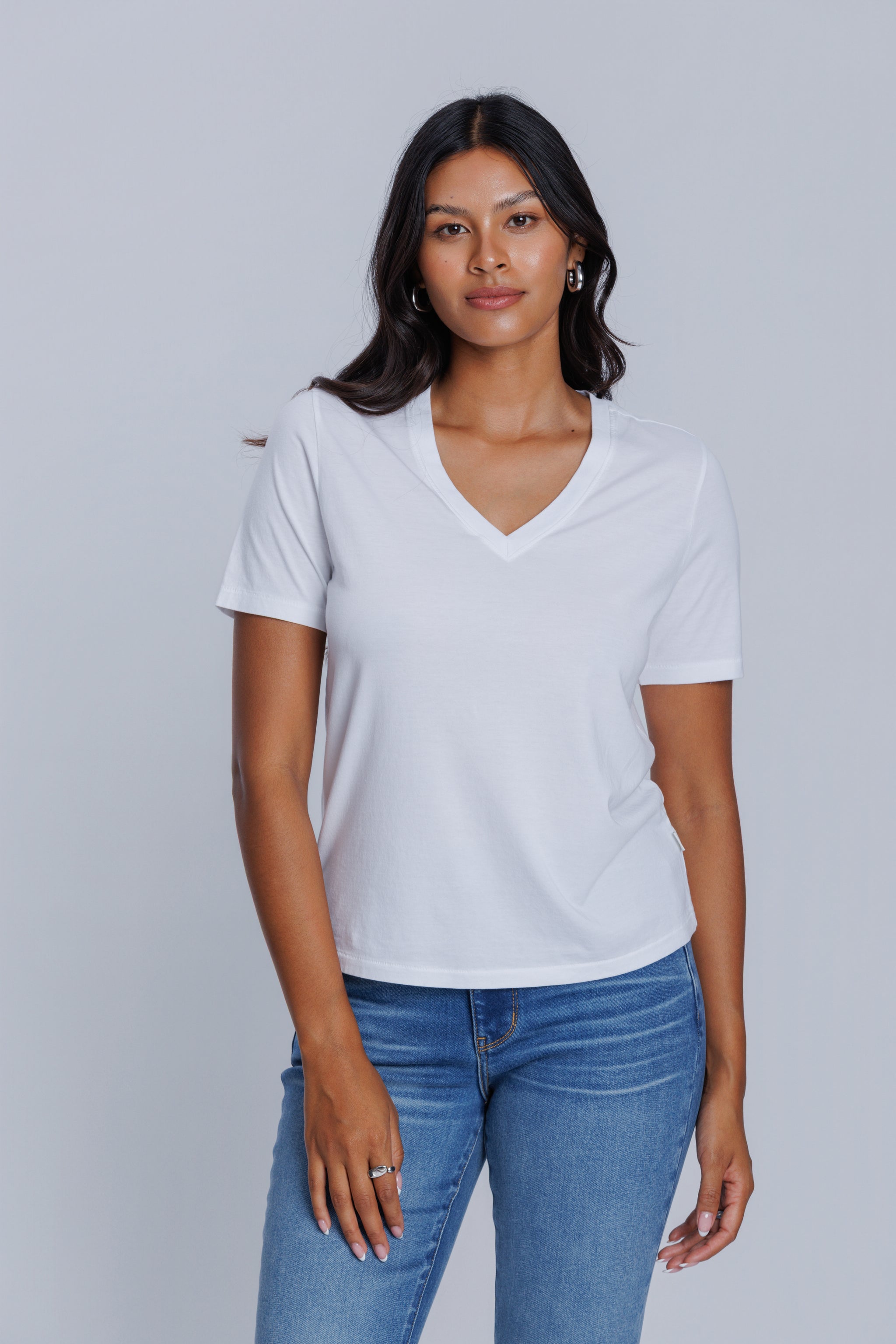 Woman wearing a DePart white t-shirt and blue skinny jeans against a light gray background | model-size: 4