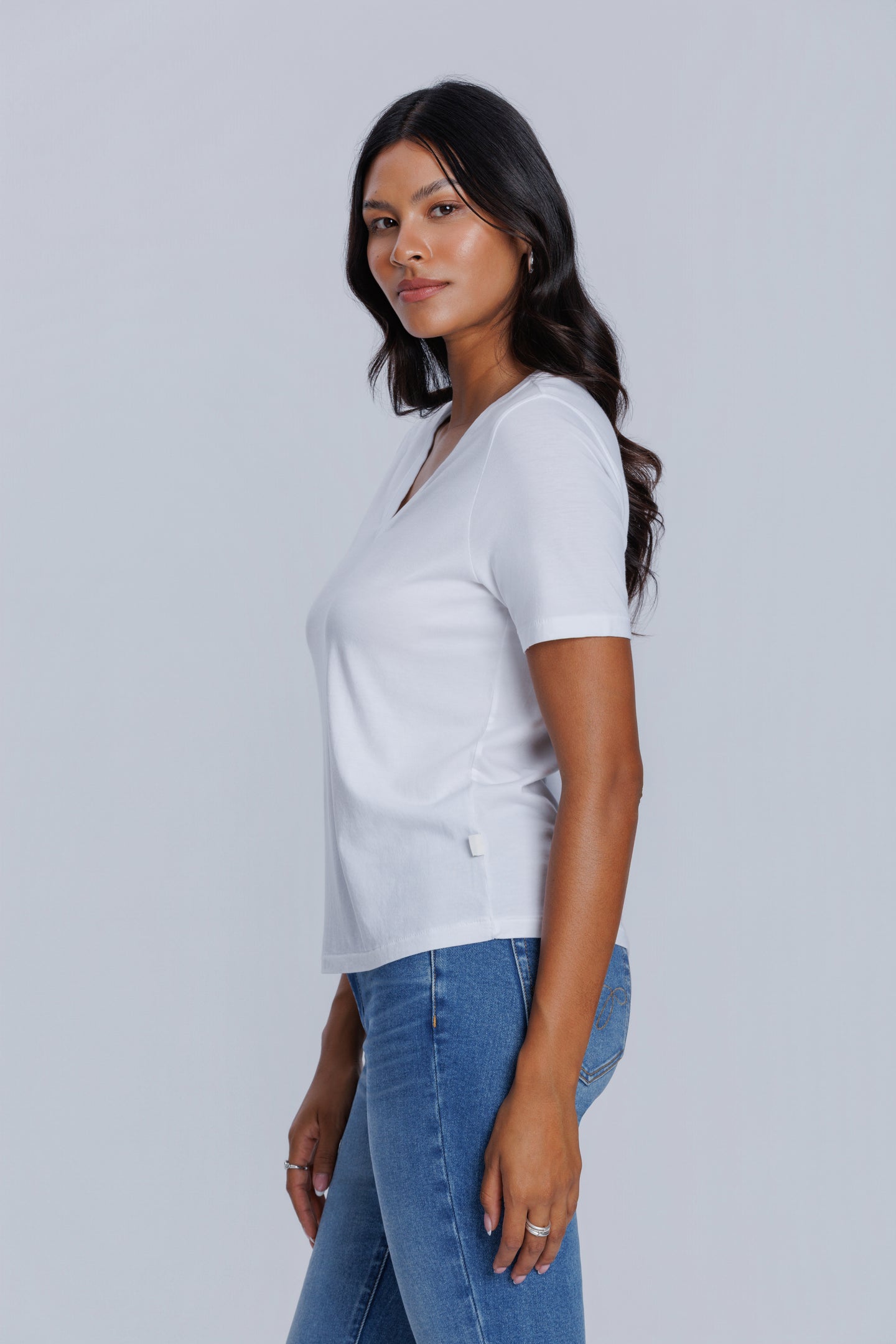 Woman wearing a DePart white t-shirt and blue skinny jeans against a light gray background