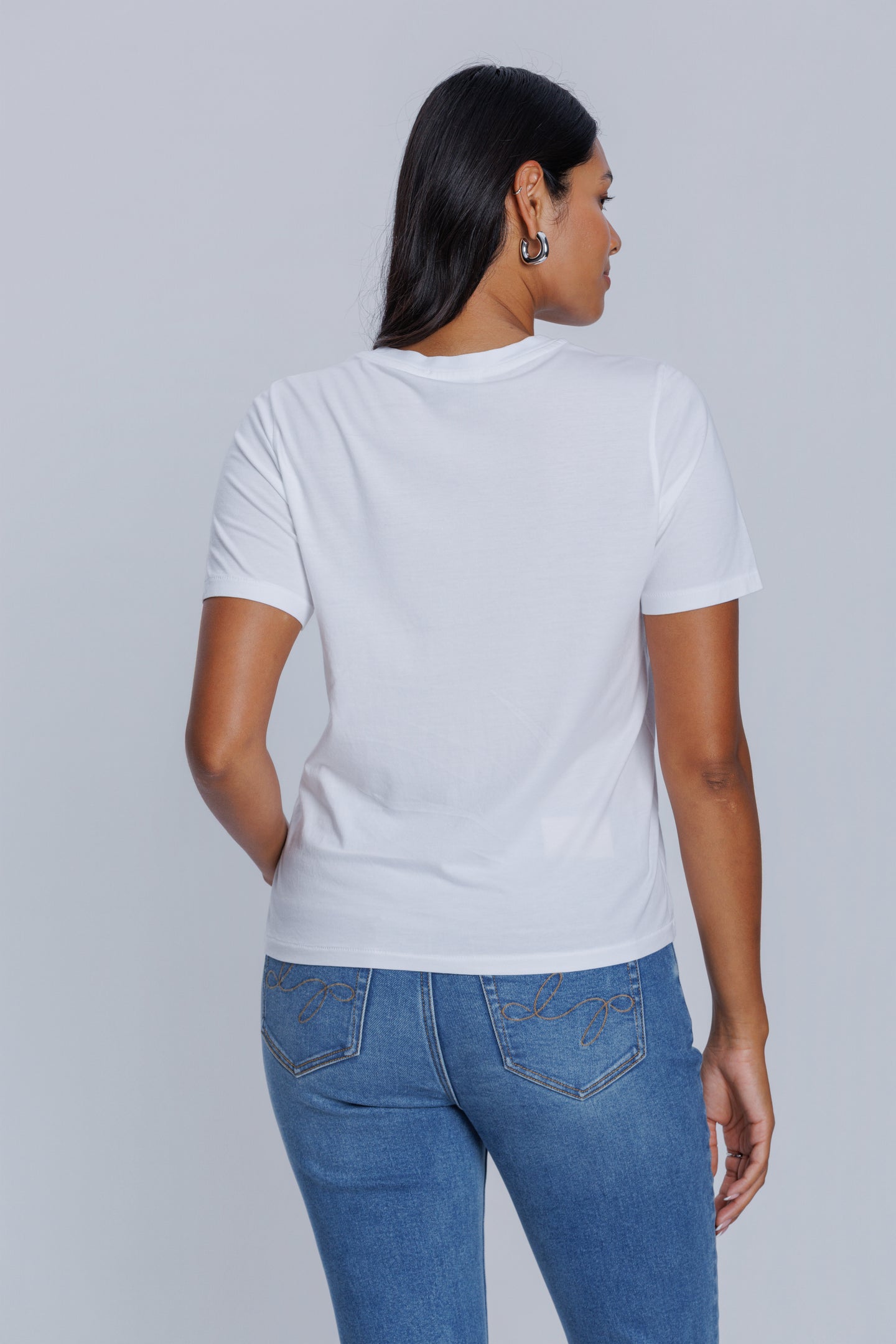 Woman wearing a DePart white t-shirt and blue skinny jeans against a light gray background