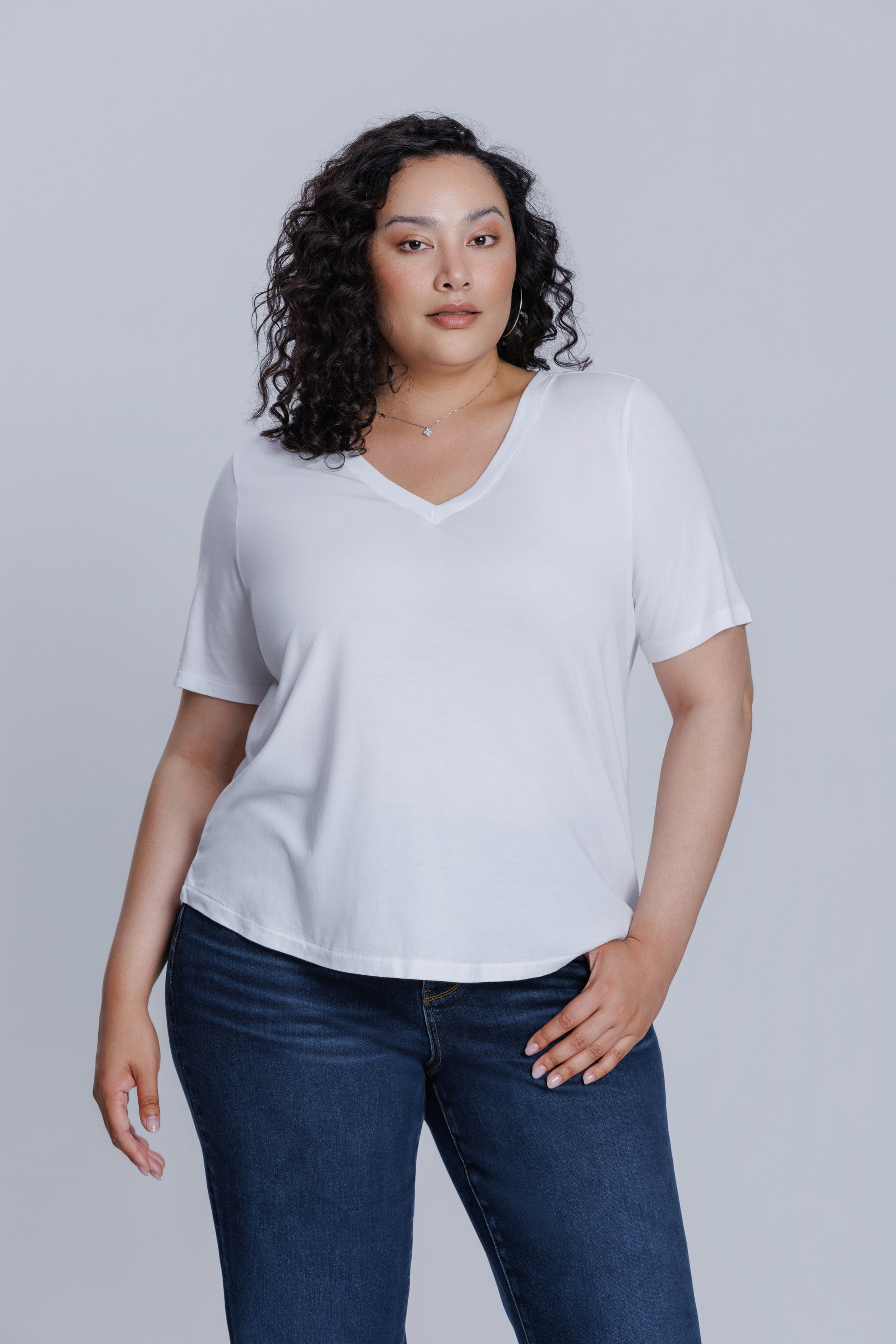 Woman wearing a DePart white t-shirt and dark blue skinny jeans against a light gray background | model-size: 16
