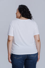 Woman wearing a DePart white t-shirt and dark blue skinny jeans against a light gray background