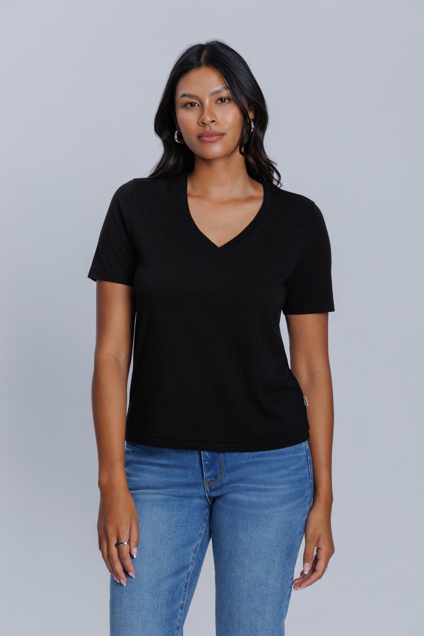 Woman wearing a DePart blackv-neck t-shirt and blue skinny jeans against a light gray background | model-size: 4
