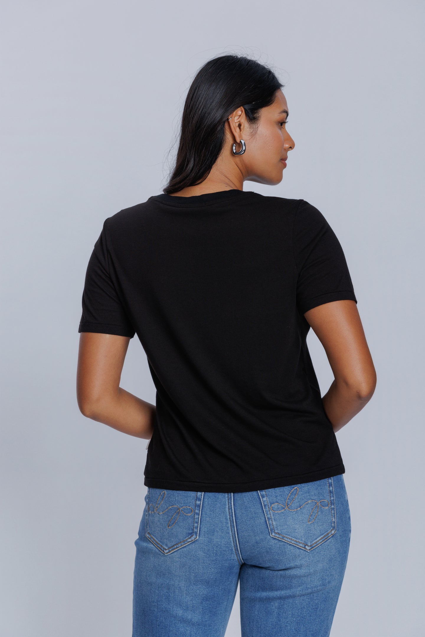 Woman wearing a DePart black t-shirt and blue skinny jeans against a light gray background